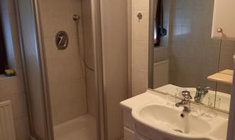 A modern bathroom with a shower cubicle and a sink. The walls are tiled and there is a large mirror.