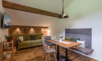 A cozy living room with a green sofa and a dining table. Large windows and warm wood create an inviting atmosphere.