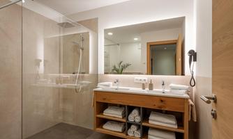 A modern bathroom with a spacious shower and a wooden sink. Fresh towels and toiletries are neatly arranged.