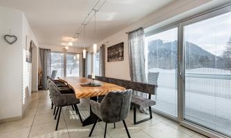 An elegant dining area with a long wooden table and upholstered chairs. Large windows provide a view of the wintry landscape.