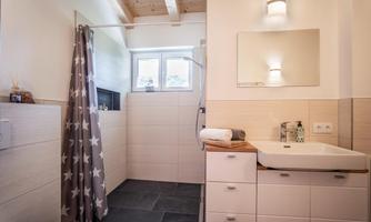 A modern bathroom with a shower and a sink. The walls are light-tiled, and there is a gray shower curtain with stars visible.