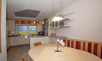 A modern kitchen with a round table and a cozy bench. Large windows provide plenty of daylight.