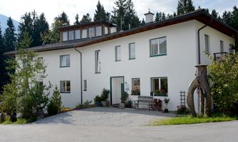 A modern house amidst trees, surrounded by a peaceful landscape. It has large windows and an inviting front door.