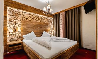 A cozy bedroom with a wooden bed and bright pillows. The wall is decorated with wooden logs and there is atmospheric lighting.