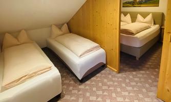A cozy room with three beds and wooden paneling. The wall is decorated with a picture of mountains.