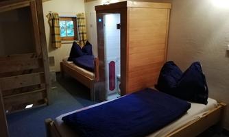 A cozy room with two beds and blue pillows. In the background, there is a sauna and a window with a view outside.