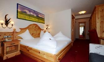 A cozy room with a wooden double bed and two large pillows. The warm interior and the alpine picture give the space a relaxed atmosphere.
