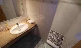 A modern bathroom with a washbasin and a large mirror. The shower has a tiled floor and is well-lit.