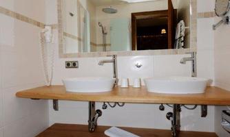 A modern bathroom with two sinks and a large mirror. The floor is tiled, and there is a towel on the wooden shelf.