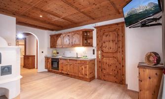 A cozy kitchen with wooden cabinets and modern appliances. The room has a warm atmosphere and a television on the wall.