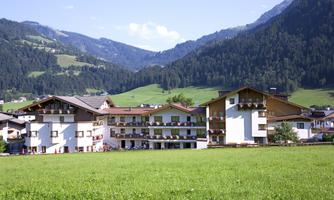 A picturesque hotel building in the Alps with green meadows and mountains in the background. The sky is clear, and the surroundings are quiet and inviting.