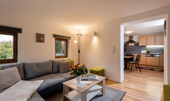 A modern living room with a gray sofa and a table. Through an open space, the kitchen is visible, which is well equipped.