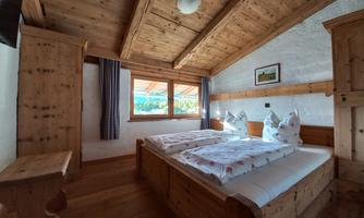 A cozy bedroom with wooden decor and two beds. Large windows provide plenty of daylight and a view outside.