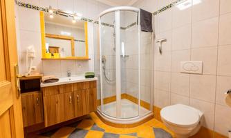 A modern bathroom with a shower, sink, and toilet. The floor is colorfully tiled, and there are wooden details in the furniture.