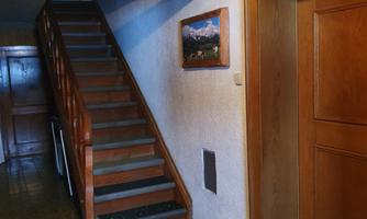 An inviting hallway with a wooden staircase and a painting on the wall. A door and a carpet are also visible.