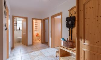 A bright foyer with white tiles and wooden details. There are several doors leading to various rooms.