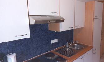 A modern kitchen with white cabinets and a blue tiled backsplash. The equipment includes a stove, a faucet, and a sink.