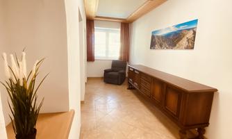 A bright hallway with a comfortable armchair and a dresser. A picture of a mountain landscape hangs on the wall.