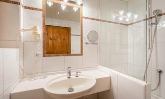 A modern bathroom with a shower, a sink, and a large mirror. The walls are tiled and well-lit.