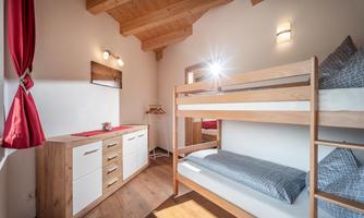A cozy bedroom with a wooden bunk bed and modern furniture. Large windows provide plenty of light and a warm atmosphere.