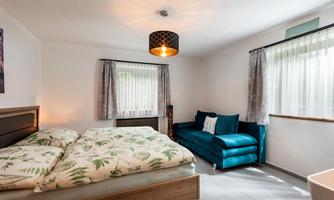A cozy bedroom with a double bed and a comfortable sofa. Bright curtains and a modern lamp create a friendly atmosphere.