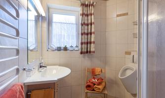 A modern bathroom with a white sink and a doorman. Towels in warm colors are placed on a chair, and there is a shower in the corner.