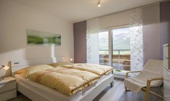 A cozy bedroom with a large bed and a beautiful view of the mountains. The room has bright colors and plenty of daylight.
