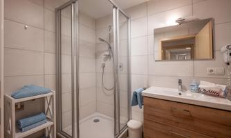 A modern bathroom with a glass shower and a double sink. There are towels on a shelf and a large mirror on the wall.