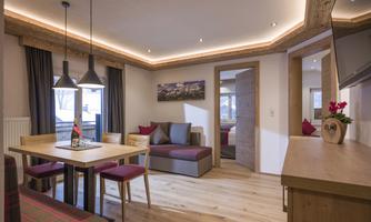A modern, inviting living room with wooden furniture and warm light accents. The space is equipped with a dining table and comfortable seating.