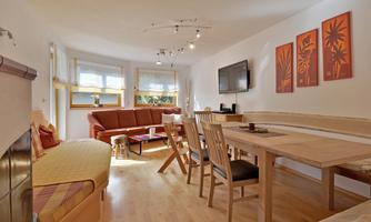 A bright and modern living kitchen with a cozy sofa and a dining area. Decorative pictures hang on the walls and there is a television.