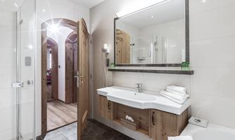 A modern bathroom with a wooden sink and a large mirror. The walls are light and the door leads to another room.