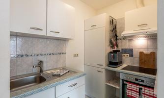 A modern kitchen with white cabinets and a stainless steel sink. The room is well-lit and contains basic kitchen appliances.