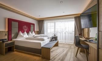 A modern hotel room with a double bed and a desk. Large windows bring a lot of light into the room.