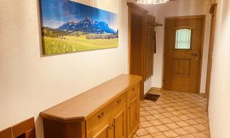 A cozy hallway with a wooden dresser and a large picture of mountains on the wall. The walls are painted light and the floor is tiled.