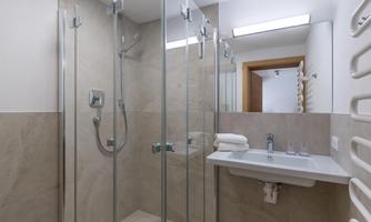 A modern bathroom with a walk-in glass shower and a minimalist sink. The walls are in neutral, light tones.