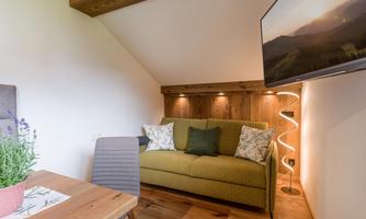 A cozy living space with a green sofa and a wooden table. A television hangs on the wall, and soft lighting creates an inviting atmosphere.