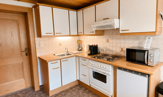 A modern kitchen with wooden shelves and bright cabinets. It is equipped with a stove, a microwave, and a refrigerator.