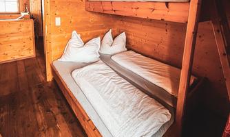 Dreibettzimmer Ein gemütliches Zimmer mit einem Etagenbett und zwei Einzelbetten. Die Wände sind aus hellem Holz und der Raum wirkt einladend. 