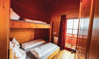 Dreibettzimmer Ein gemütliches Zimmer aus Holz mit einem Etagenbett und einem Einzelbett. Große Fenster lassen viel Licht herein und bieten einen Blick nach außen. 