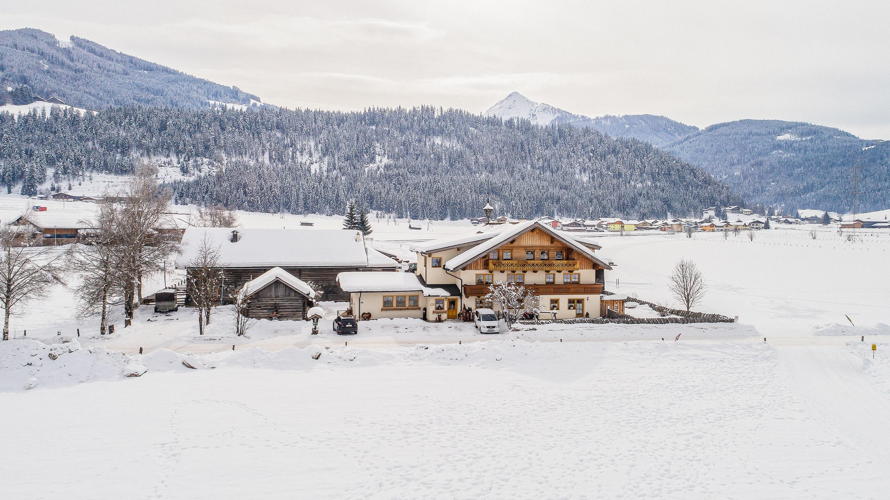 A picturesque winter landscape with snow-covered fields and a traditional chalet. In the background, mountains and a calm sky can be seen.
