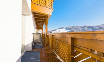 A beautiful wooden balcony with a view of snow-covered mountains. The sky is clear and blue.