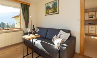 A cozy living room with a gray sofa and a table. On the table, there are two wine glasses and a bottle of wine, while a beautiful landscape painting hangs on the wall.