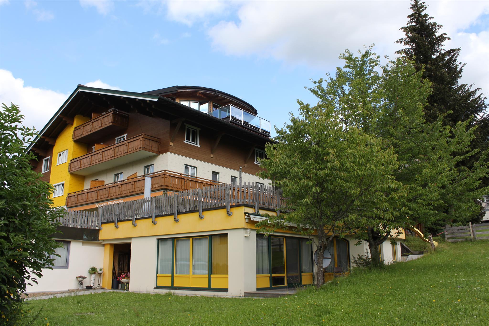 A modern building with several floors and a large balcony.  
Surrounded by grass and trees, it radiates a calm atmosphere.