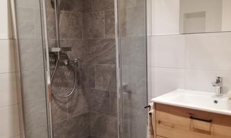 A modern shower with glass walls in a bathroom. The room has a bright color scheme and a stylish wooden washbasin.