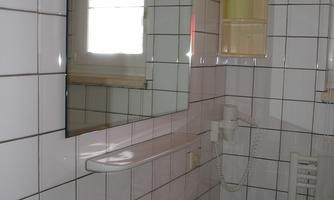 A modern bathroom with white tiles and a sink. A mirror and a window provide additional light.