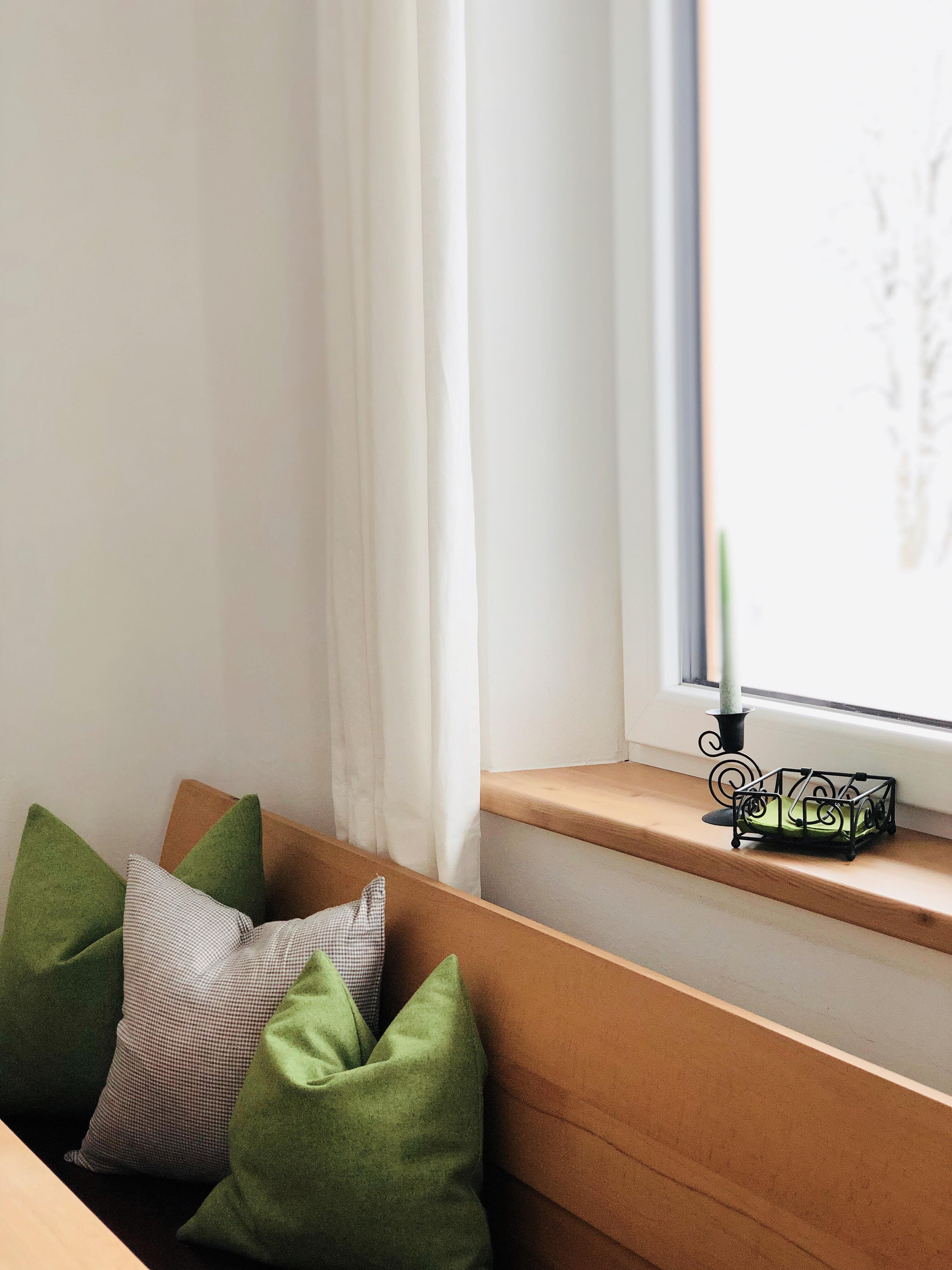 A cozy seating area with green and gray cushions. On the windowsill, there is a small candle holder with a green candle.