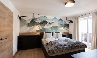 A modern bedroom with a large bed and an artistic mountain wall.   
Large windows provide plenty of daylight and a cozy atmosphere.