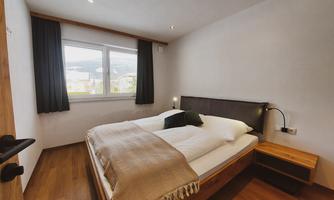 A modern bedroom with a double bed and wooden floor. Bright windows provide plenty of daylight.