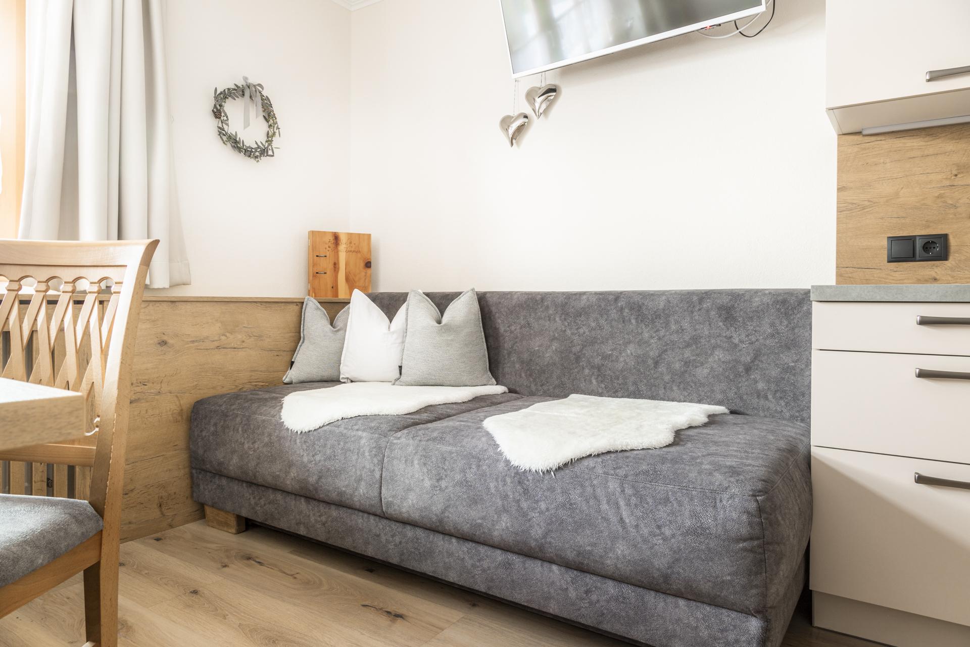 A modern living room with a gray couch and decorative pillows. The wooden elements and the TV give the room a cozy atmosphere.