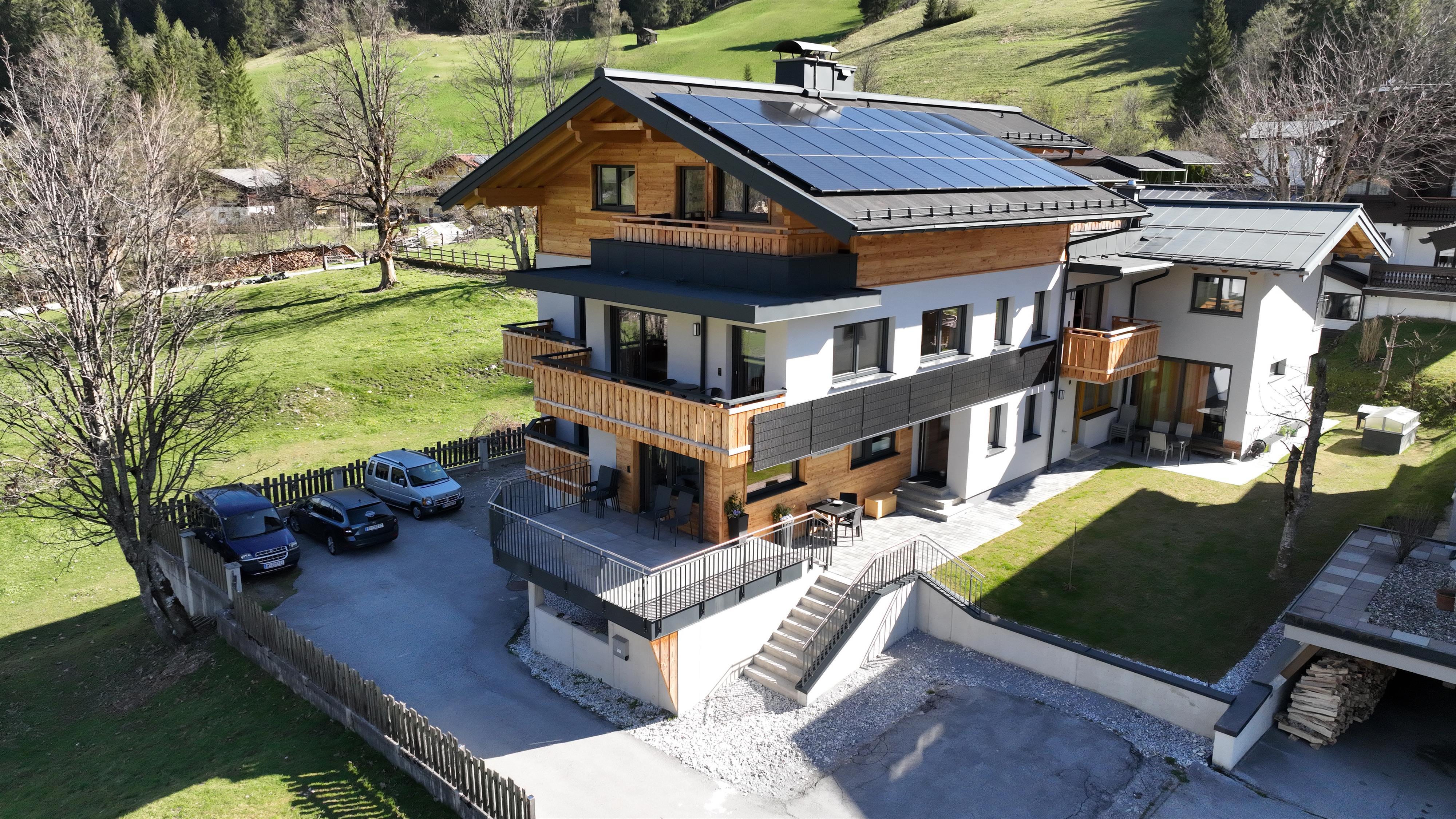 A modern house with multiple floors, rooms, and apartments with balconies. It is located in a green area with trees and meadows.  
Ample free parking available.